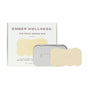 A rectangular box labeled Ember Wellness The Body Serum Bar Set is shown with a metal tin and a wavy-edged beige bar, both displaying EMBER—ideal for deeply hydrating and nourishing sensitive skin.
