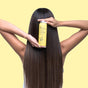 Against a light yellow background, someone with long, shiny brown hair—perfect for fine hair—holds a yellow bottle of Hydrating Volume Conditioner by The Powder Shampoo to their head and back.