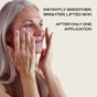 A smiling older woman with long gray hair gently touches her cheeks. Text reads, “Experience instantly smoother, brighter, lifted skin after just one use of Ember Wellness The Serum Bar.”.
