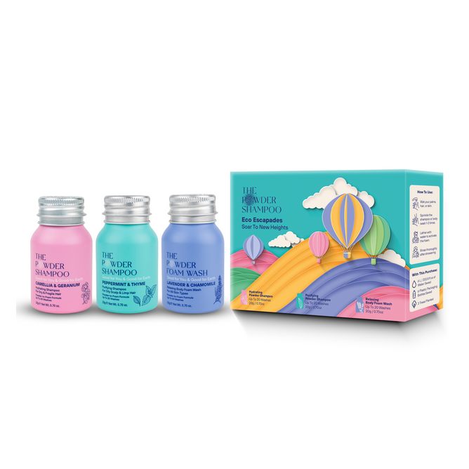 Three colorful bottles of The Powder Shampoo and Foam Wash stand beside the Soar to New Heights travel set box, featuring Cappadocia hot air balloons and a rainbow on a pastel sky. Pink, blue, and teal bottles have silver caps.