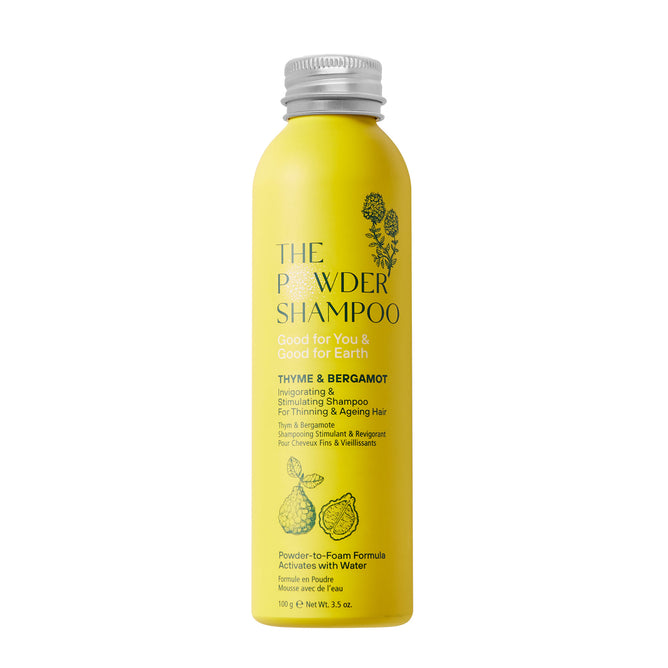 The Invigorating & Stimulating Powder Shampoo, in a yellow cylindrical aluminum bottle with thyme and bergamot illustrations, promises benefits for thinning and aging hair. Its 100g (3.5 oz) powder-to-foam formula is enriched with biotin for hair growth and activated with water. The bottle is recyclable.