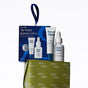 The Winter Hydration Gift Set features a lip treatment tube and a dropper bottle of serum resting on a patterned green gift box tied with a navy blue ribbon.