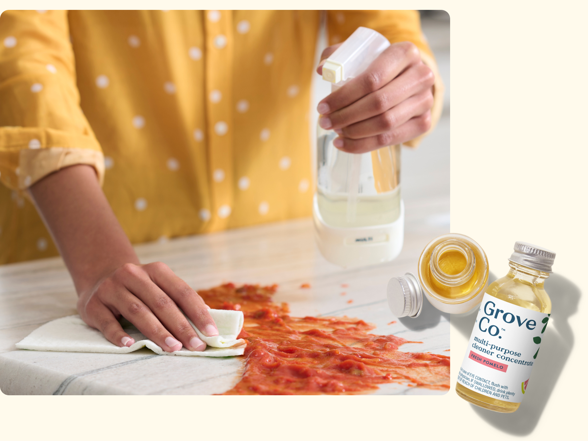 A person in a yellow shirt sprays cleaner and wipes up a large pizza sauce spill on a white countertop. In the corner, there are bottles of Grove Co. all-purpose cleaner concentrate.
