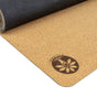 A partially rolled open Nomad Air Cork Yoga Mat by Yoloha Yoga, featuring a non-slip, eco-friendly cork surface with a black underside. This portable mat displays a circular floral Yoloha logo with the word “YOGA” printed near one corner.