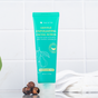 A turquoise tube of Tree To Tub Gentle Exfoliating Face Wash & Cleanser with Salicylic Acid & Natural Micro-Exfoliators sits upright on a bathroom counter. Its labeled fragrance-free with a soapberries illustration. Nearby, there’s a small heap of soapberries and folded towels on the white surface.