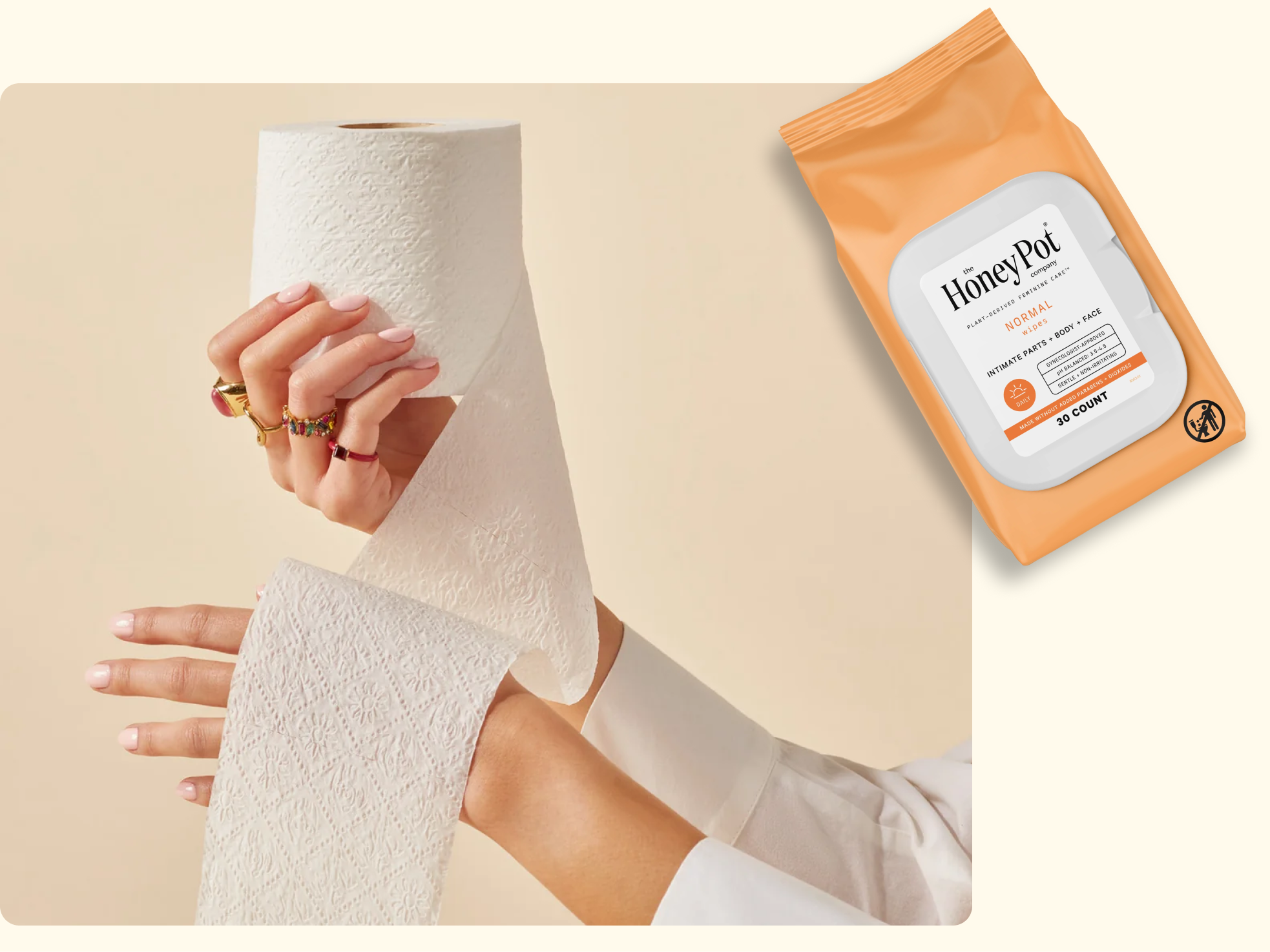A person’s hands holding a roll of toilet paper, with one hand pulling the paper. Next to it is a package of Honey Pot intimate wipes on a light background.