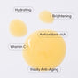 Four yellow serum droplets labeled Hydrating, Brightening, Antioxidant-rich, Vitamin C, and Visibly Anti-Aging highlight the benefits of Uncommon Beauty’s Enhanced Pineapple Peptide Nectar hydrating vitamin C serum. White background.