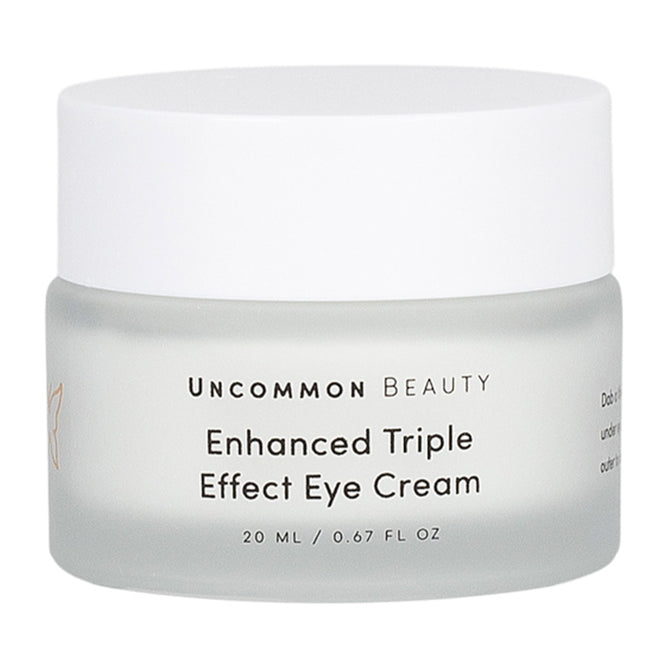 A frosted glass jar with a white lid labeled “Uncommon Beauty Enhanced Triple Effect Eye Cream” in black text, 20 ml (0.67 fl oz), featuring super ingredients for under-eye care.