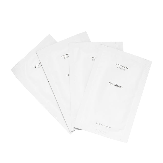 Four white single-use Uncommon Beauty Eye Masks packets are fanned out on a white background, offering a refreshed look and youthful glow.