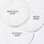 Three overlapping white textured exfoliating pads from Uncommon Beautys Glycolic Pads are labeled with Salicylic Acid, Glycolic Pads, and Witch Hazel, linked by a curved arrow to suggest pore-minimizing synergy on a clean white background.