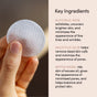 A hand holds a round exfoliating pad. Text reads: Uncommon Beauty Glycolic Pads feature glycolic and salicylic acids to help minimize pores, while witch hazel offers added skincare benefits.