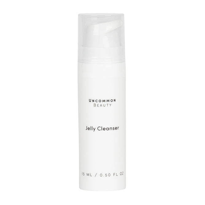 A white cylindrical bottle labeled Mini Jelly Cleanser by Uncommon Beauty, with a clear cap and minimalist black text. This gentle, fragrance-free daily face cleanser contains 15 ml (0.5 fl oz) and has a plain background.