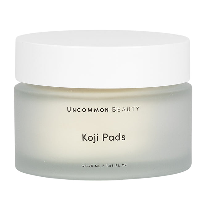 A frosted glass jar with a white lid labeled Uncommon Beauty Koji Pads, holding 48.48 ml (1.63 fl oz) of skin perfector designed to brighten and enhance your complexion.