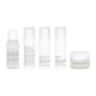 Five Uncommon Beauty Daily Skincare Travel Set containers—one clear bottle, three white pump bottles, and a jar with minimalistic labels—arranged on a white background, ideal for travel or clean skincare routines.