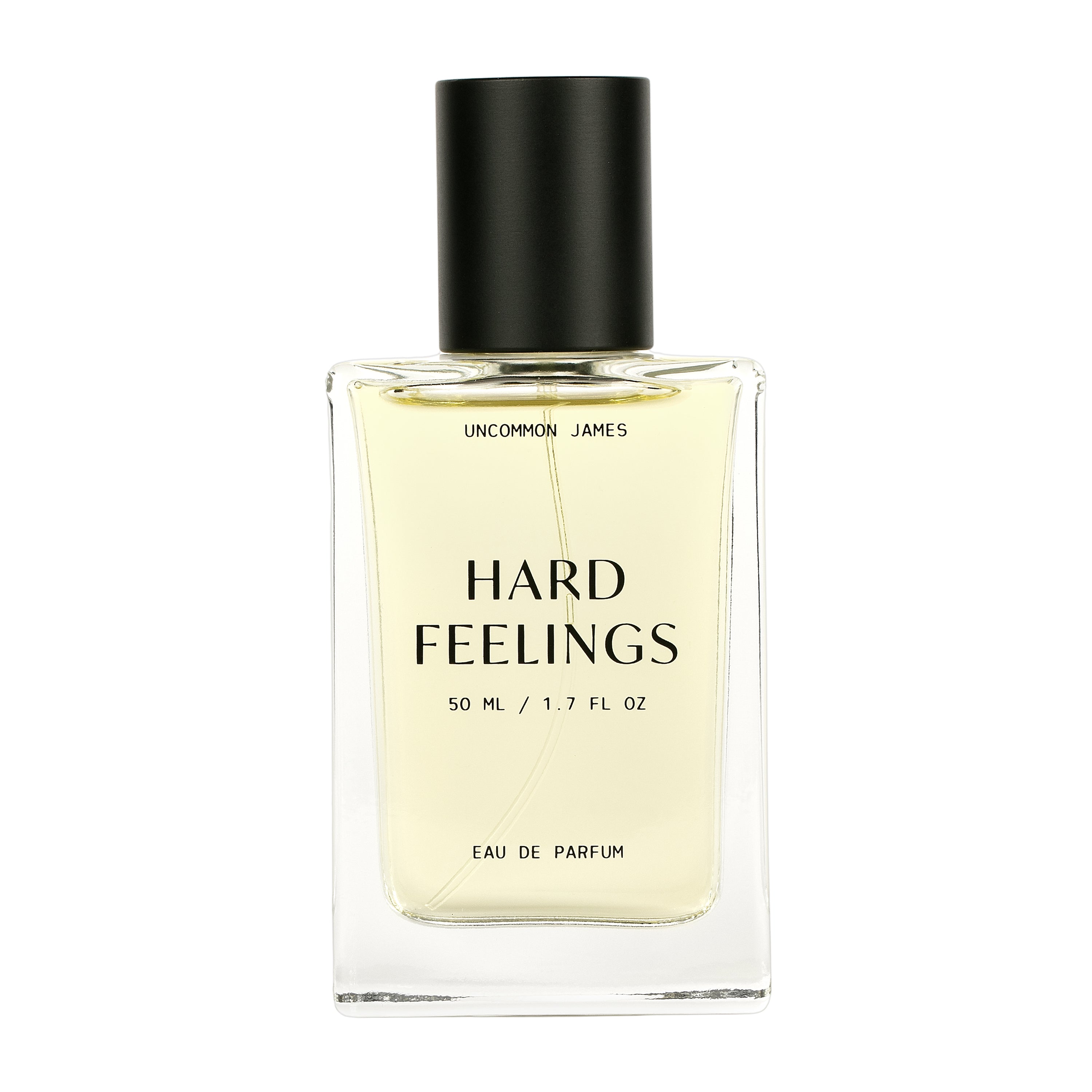 A clear glass bottle of Hard Feelings Eau de Parfum by Uncommon Beauty features a black cap and label noting 50 ML / 1.7 FL OZ. The pale yellow liquid promises a captivating sandalwood and incense scent.