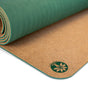 The Unity Pro Cork Yoga Mat by Yoloha Yoga is a rolled-up, sustainable yoga mat with a green wavy textured top and a cork underside featuring a green lotus logo in the corner.
