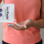 Wearing a coral shirt, a person pours Unpaste Fluoride Mint Toothpaste Tablets from a packet into their hand, showcasing an easy and eco-friendly oral care alternative.