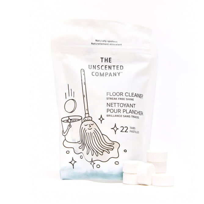 A white package of The Unscented Company Floor Cleaning Tabs, decorated with a black line drawing of a mop, bucket, and clean floor. In front are four fragrance-free and dye-free tabs designed for effective floor cleaning.