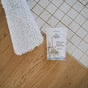 A packet of The Unscented Company Floor Cleaning Tabs sits on the edge of a tiled and wooden floor, beside a white microfiber mop.