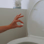 A hand holds The Unscented Company’s Toilet Bowl Cleaning Tab - Unscented above an open toilet in a clean, minimalistic bathroom, showcasing a simple approach to sustainable hygiene.