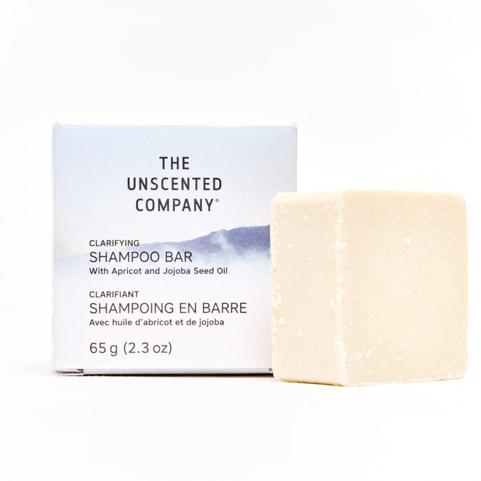 A rectangular box labeled The Unscented Company Shampoo Bar stands beside a beige, square shampoo bar. The plastic-free box highlights apricot and jojoba seed oils and features English and French text.