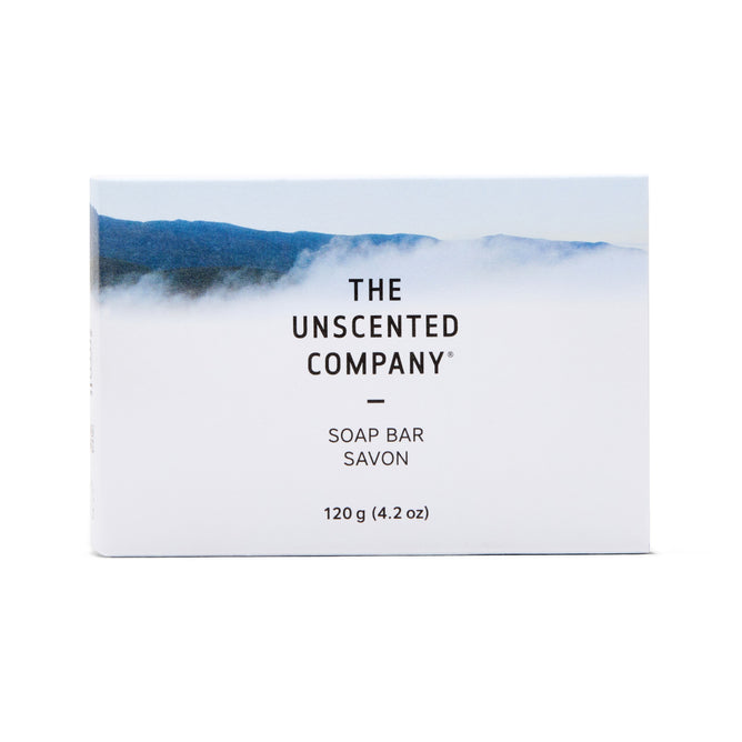A white Soap Bar box from The Unscented Company features a misty blue mountain landscape, black text reading “Soap Bar Savon 120 g (4.2 oz),” and highlights its fragrance free formula.