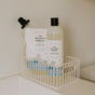 A bottle and the Kids Big Bubble Bath Refill Bag by The Unscented Company rest in a white metal basket on a bathroom surface, with labels showing playful illustrations of a baby in gentle bubbles.