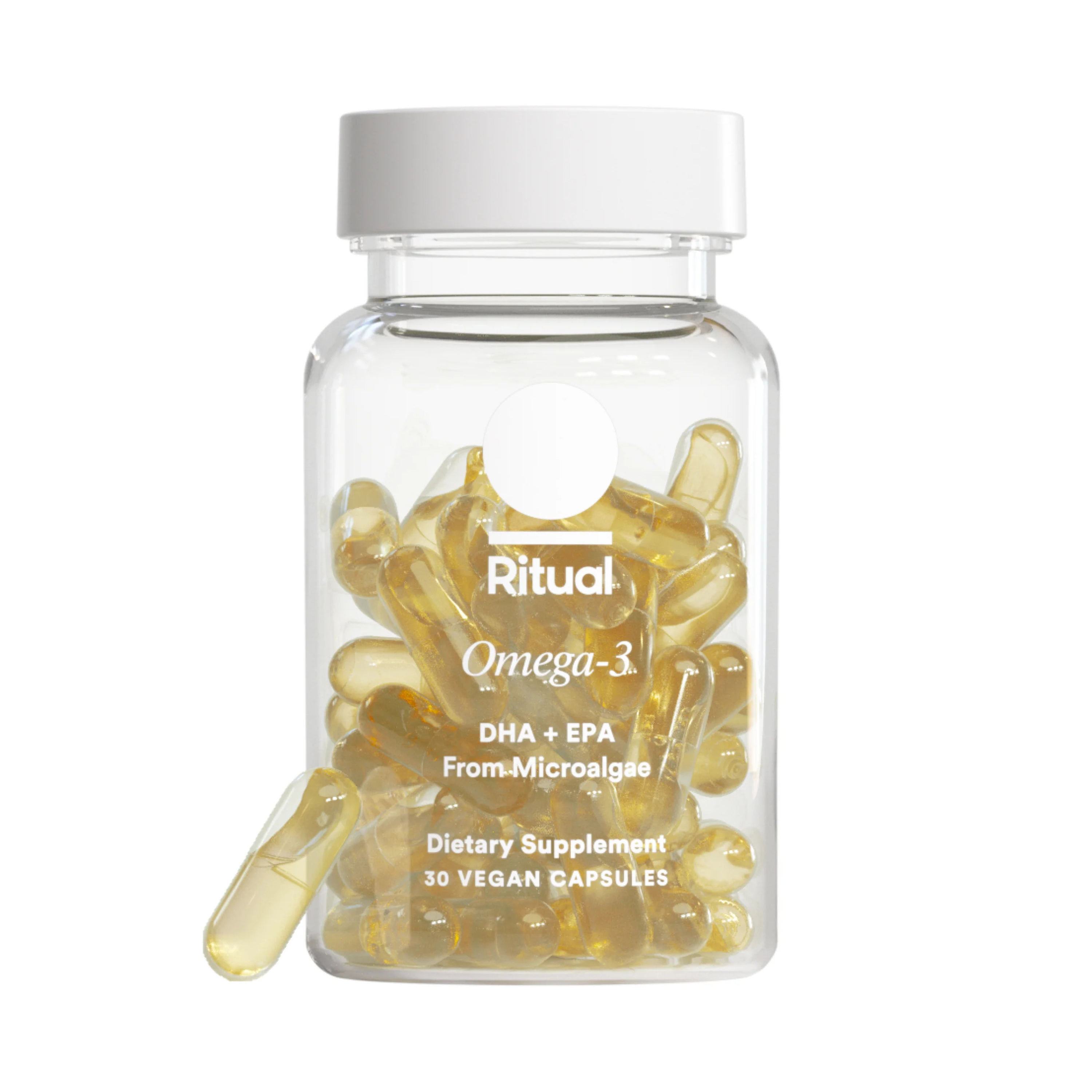 A clear bottle labeled Ritual Omega-3 contains yellow vegan capsules. The label mentions DHA + EPA from microalgae, dietary supplement, and 30 vegan capsules. One capsule lies outside the bottle.