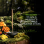 A Murphys Naturals Ceramic Incense Stick Holder displays a single incense stick atop moss with orange flowers, lush ferns, and natural pest control scenery. Text: Made exclusively to hold Murphys Naturals incense sticks.