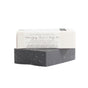 A black rectangular Activated Charcoal Facial & Body Bar by Little Seed Farm, partially wrapped in white packaging labeled for sensitive and acne-prone skin, rests on a plain white background.