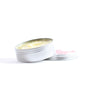 An open tin of Little Seed Farm’s Hand-Aid Healing Hand Balm sits on a white surface, showing its yellow organic balm inside. The small, round silver metal lid rests beside the container.