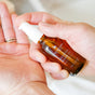 A person pours Little Seed Farm Beard Oil from a brown glass bottle into their palm, getting ready to use this moisturizer for softer, well-groomed facial hair.