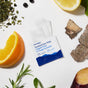 A packet of Ursa Major Essential Face Wipes, Individually Wrapped, with an open wipe is surrounded by slices of lemon, orange, beet, some bark, herbs, and blackberries on a white background.