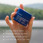 A hand holds a blue jar of Ursa Major Golden Hour Recovery Cream against a blurred outdoor background, with text listing its benefits: it nourishes skin, deeply hydrates, soothes, and helps soften fine lines.