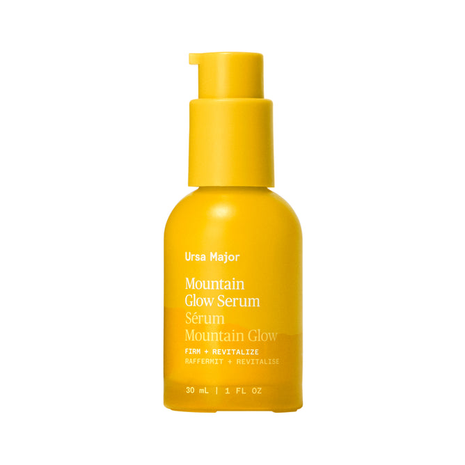 A 30 mL (1 fl oz) yellow bottle of Ursa Major Mountain Glow Serum with pump dispenser, labeled Firm + Revitalize, offers rejuvenating skin nutrition.