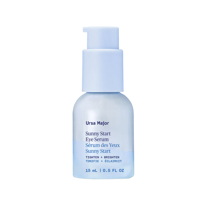 A pale blue bottle of Ursa Major Sunny Start Eye Serum features a convenient pump dispenser. The label displays product details in both English and French, indicating that the bottle contains 15 ml (0.5 fl oz). This de-puffing eye treatment is specially formulated to help reduce dark circles, promoting a brighter and more well-rested appearance.
