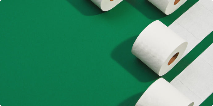 Four white toilet paper rolls are partially unrolled and arranged diagonally on a smooth green background, creating a visually clean and organized composition.