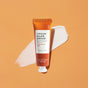 The Pumpkin Pie Vegan Hand Crème 1.5 oz by VOESH, featuring pumpkin extract and allergen-free fragrance, is shown on an orange background with a swipe of white cream beneath the tube.