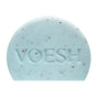 The VOESH Body Buffing Bar With AHA is a light blue, half-circle exfoliator with dark specks and “VOESH” engraved on the front.