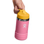 A hand holds a Hydro Flask Kids Stainless Steel Wide Mouth Bottle, 12 oz, in pink. This BPA-free bottle features double-wall vacuum insulation, a yellow cap with a white logo, a carry ring on top, and a sleek silver band around the neck for style and functionality.