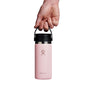 A hand holds a pink 16 oz Hydro Flask Wide Mouth Bottle with Flex Sip Lid™ against a white background. The stainless steel bottle boasts TempShield double-wall vacuum insulation and features the Hydro Flask logo.