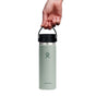 A hand holds a light green Hydro Flask Wide Mouth Bottle designed for coffee and tea, featuring the TempShield double-wall insulation. The 20 oz stainless steel bottle, with its iconic logo, is gripped by the black strap of the Flex Sip Lid™ and stands out against a plain white background.