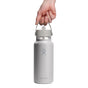 Against a white background, a person holds a sturdy Hydro Flask Wide Mouth Bottle, 32 oz, in white, featuring the iconic logo. The bottle includes double-wall insulation and a leakproof Flex Straw Cap for ultimate convenience.