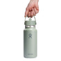A hand holds a green Hydro Flask Wide Mouth Bottle with Flex Straw Cap, 32 oz, against a white background. Known for double-wall insulation, it features the brands logo and a convenient screw-on lid.