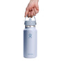 A hand holds a light blue 32 oz Hydro Flask Wide Mouth Bottle with Flex Straw Cap, showcasing the brands logo in blue. Against a plain white background, it features double-wall insulation to keep drinks cold or warm.