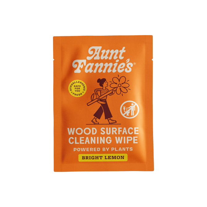 An orange packet labeled “Aunt Fannie's Wood Surface Cleaning Wipe - Sample.” The packaging features a no-wax formula, icons, and an image of a person holding a large lemon slice.