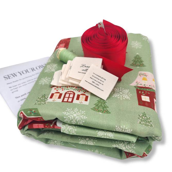 The Sew Your Own Set of 10 Gift Bags – Folk Art Cottages by Waste Free Celebrations includes festive green fabric, thread, labels, instructions, and red ribbon—ideal for your next reusable Christmas gift bag craft.