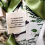 Close-up of a fabric label on a floral-patterned, 100% cotton bag from the Waste Free Celebrations Set of 5 Reusable Gift Bags - Natural Noel Birdlife. The label says: Do not throw me out. Return me or reuse me. Green ribbon accents the top.