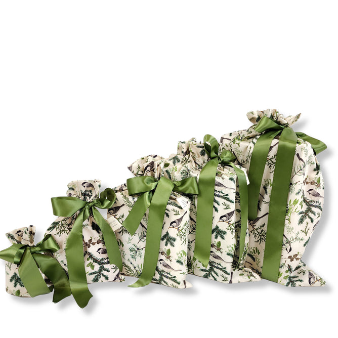 The Waste Free Celebrations Set of 5 Reusable Gift Bags - Natural Noel Birdlife features cotton bags with bird and greenery prints, green satin ribbons, and are displayed in a row from smallest to largest on a white background.