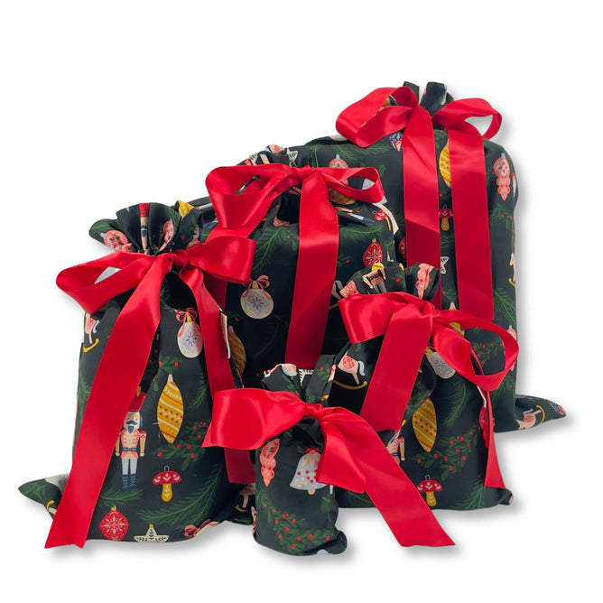 Set of 5 Reusable Gift Bags - Folk Art Ornaments by Waste Free Celebrations, featuring festive holiday prints with ornaments and nutcrackers, each topped with a red ribbon bow—perfect for sustainable Christmas gift wrapping.